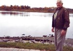 Billy Martin Jr. stands on the site of the old Russel Marine Railway, with timbers still visible in the foreground. Billy worked alongside his father, Capt. William Martin, on the Hallett, starting at 25 cents an hour. Looking south across the Rainy River between Crowe and Armit Avenues.
